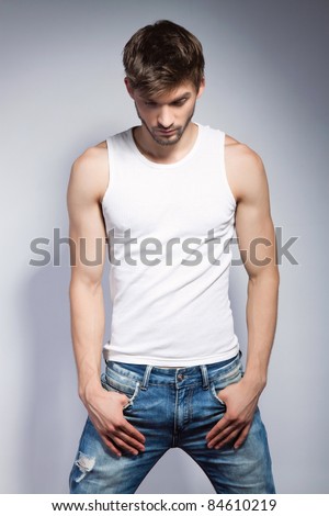 Fashion portrait of the young beautiful man in white t-shirt posing over gray background, series photo