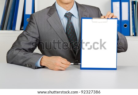 businessman holding a blank white board, signboard, clipboard with paper, point finger with pen on an empty bill board with copy space for text, unrecognizable person sitting at the desk at office