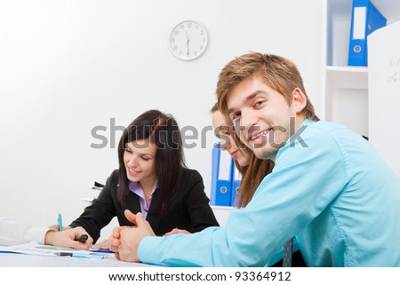 portrait of a handsome young man happy smile. Sitting at the desk at office with business colleagues people in the background businesspeople working, businessman looking at camera,