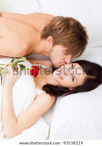 Man giving a rose and a kiss to his beautiful wife in bed, young lovely couple lying in a bed, happy smile love, girl looking at camera, top above view