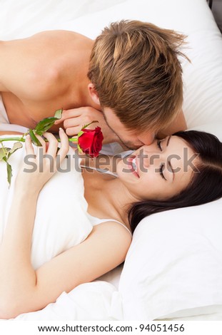 Man giving a rose and a kiss to his beautiful wife in bed, young lovely couple lying in a bed, happy smile love, girl with closed eyes, top above view