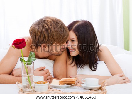 happy young couple eat breakfast in bed in morning with red rose flower, lovely couple lying in a bed, happy smile kissing, concept of honeymoon, valentine day