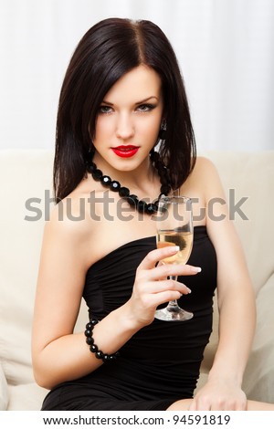 Portrait young woman with glass of champagne, girl with red lips wear evening dress, glamour vogue style, sensual looking at camera, sitting indoors
