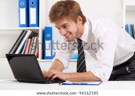Successful excited young business man using laptop, happy smile sitting at the desk, handsome businessman working on computer