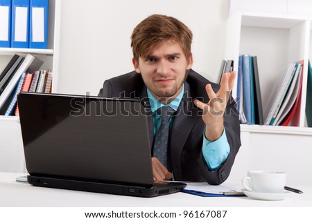 Angry business man hand gesture sitting at desk in office, portrait of young handsome businessman looking at camera, concept of executive yelling, conversation problem communication crisis