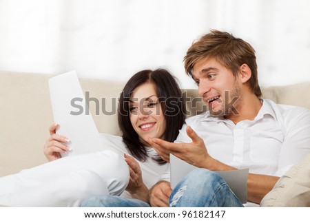Happy couple reading a letter in their living room, young smile man and woman sitting on couch, sofa