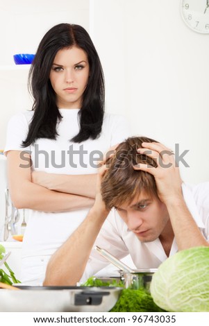 portrait of young couple conflict in their kitchen, relationship problem, negative emotion, angry woman with folded hands looking to sad man