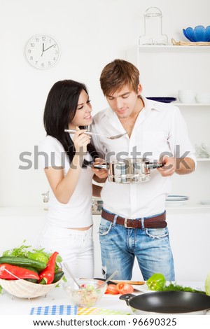portrait of young couple cooking, tasting a meal in their kitchen happy smile, hold pan spoon with ready meal, soup, boiler