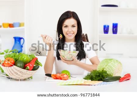 Portrait of a young woman eating a salad in her kitchen, while cooking, happy smile looking at camera