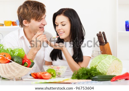 portrait of young couple tasting the meal in their kitchen happy smile, man feed woman with spoon, looking to each other