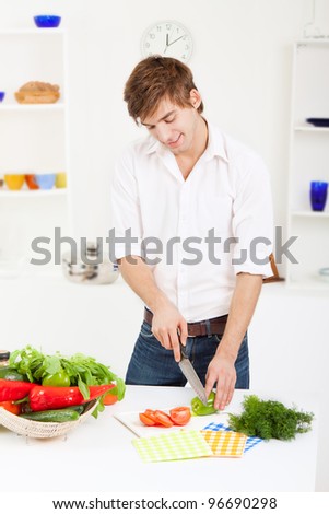portrait of handsome young man cooking slice, cutting green pepper, tomato in the kitchen, cooking, prepare vegetable salad, happy smile