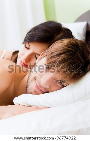 young lovely couple lying in a bed, happy smile man looking at camera, woman sleep with closed eyes