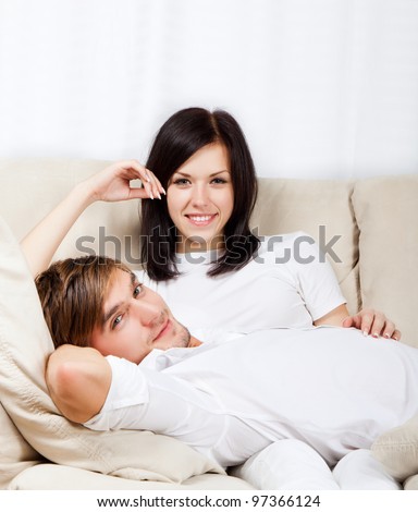 beautiful young happy couple laying on couch happy smile looking at camera, portrait of lovely young man and woman hug, embrace on the sofa