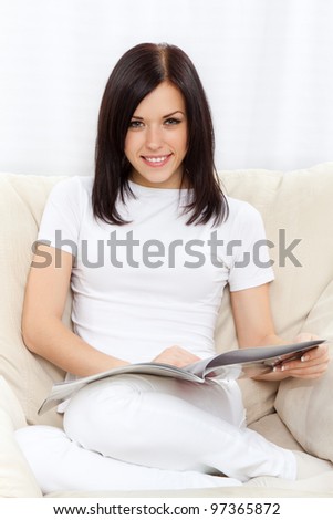 Young happy smile woman read magazine on sofa in living room,  at home - indoors, sitting on chair