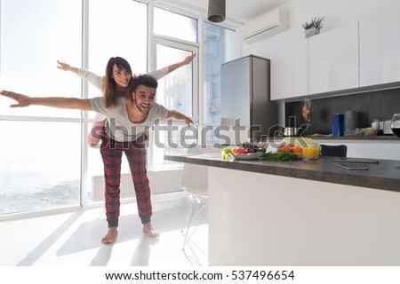 Young Couple In Kitchen, Lovers Hispanic Man Carry Asian Woman Modern Apartment With Big Windows Interior