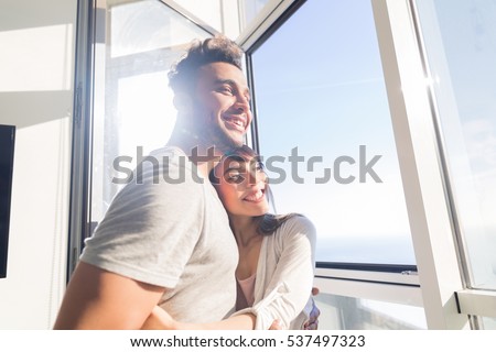 Young Couple Embrace Modern Apartment Big Panoramic Window Sea View, Mix Race Man And Woman Morning Home Interior