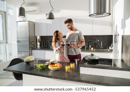 Young Couple Embrace In Kitchen, Hispanic Man And Asian Woman Hug Drink Wine Modern Apartment Interior