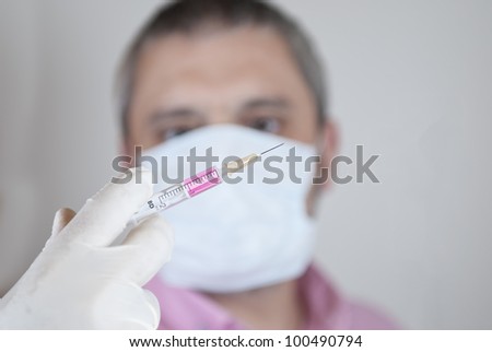 Scientific protected with mask and gloves holding a syringe filled with fluid in his laboratory.
