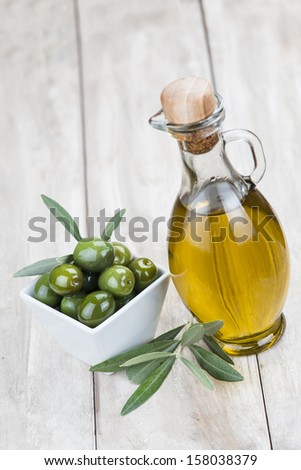 A glass bottle of olive oil and green olives on a wooden background
