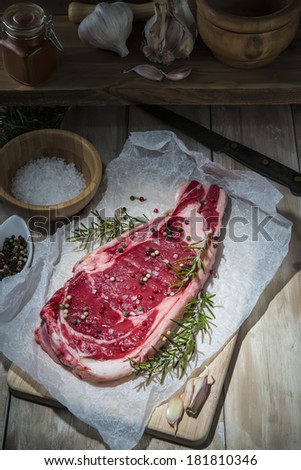 Raw steak garnished with pepper, rosemary, and garlic on the table of the kitchen