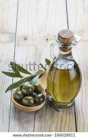 A glass bottle of olive oil and a wooden spoon with  olives on a table