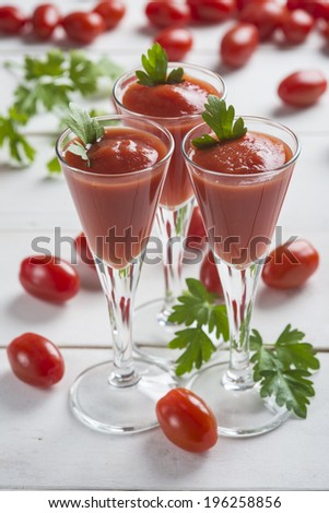 Tomato juice cocktails garnished with parsley leaves on a white wooden background and cherry tomatoes