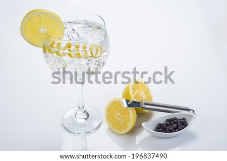 Gin and tonic in a highball cup garnished with a lemon wedge and twist