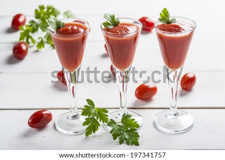 Tomato juice cocktails garnished with parsley leaves on a white wooden background and cherry tomatoes