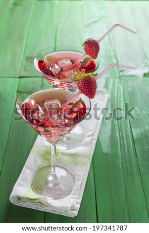 Red martini cocktail with strawberries on a green wooden background