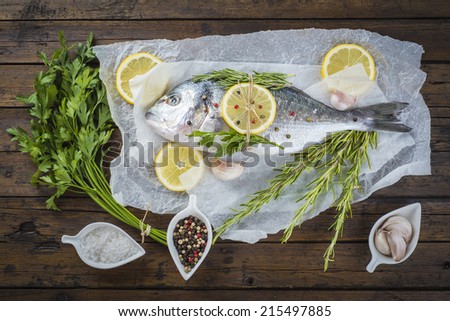 Fresh gilt-head sea bream fish with herbs and spices on a bakery release paper ready to be cooked