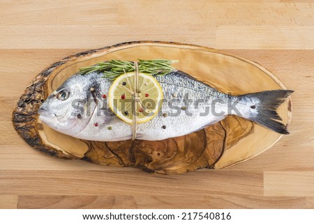 Raw gilt-head sea bream with spices and herbs on a cutting board ready to be cooked