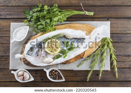 Raw gilt-head sea bream with herbs and spices in a bakery release paper prepared to be cooked