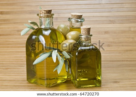 Three bottles of olive oil and some olives on a bamboo mat.