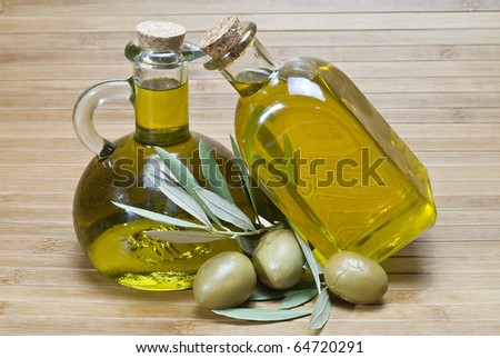 Two bottles of olive oil and some olives on a bamboo mat.