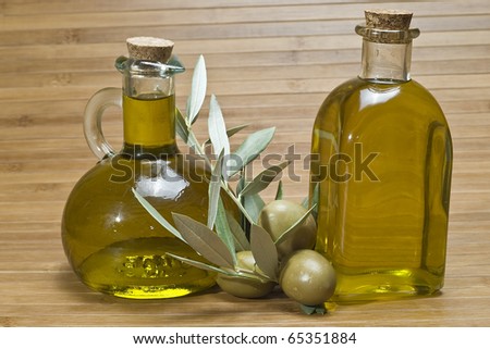 Two different bottles of olive oil and some olives on a bamboo mat.