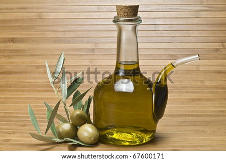 A bottle of olive oil and some olives on a bamboo mat.