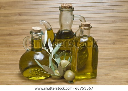 Some bottles of olive oil and some green olives on a bamboo mat.