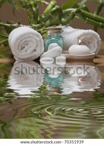Spa background with bamboo plants, towels, candles and bath salts in green reflected on water.
