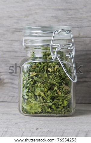 A jar with parsley on an old wooden stand.