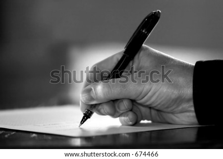 Hand at desk signing paperwork/document/contract or making notes - Black and White image.