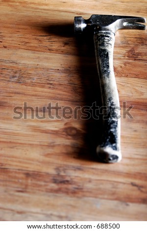 A well-used construction hammer lying on a distressed wood floor represents experienced construction, remodeling, or do-it-yourself projects.
