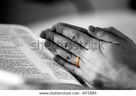 stock photo Man's hands in prayer over a Holy Bible with a gold wedding