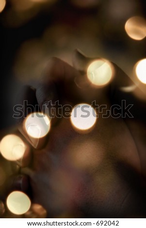 Blurred Christmas tree lights with praying hands blended into image - represents faith and spirituality in the Christmas/Holiday season.