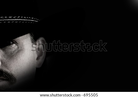 Half-face portrait of a cowboy in black hat against black background with shadow and light effect.