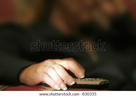 Woman sitting with a finger in blurred motion on a remote control device - can represent technology and/or a couch potato metaphor.