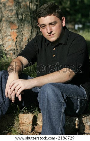 College-aged Caucasian male sitting outdoors in sunlight â€“ serious expression.