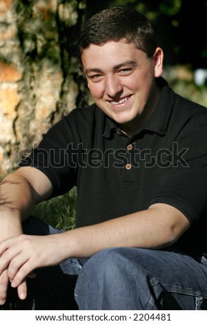 College-aged Caucasian male smiling outdoors in natural light (shallow focus).