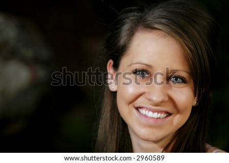 A smiling, attractive, college-aged woman outdoors with dramatic lighting (shallow focus).