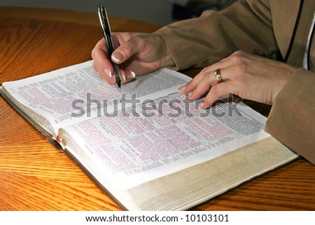 A woman studies a Holy Bible alone at a table (Christian image, shallow focus).