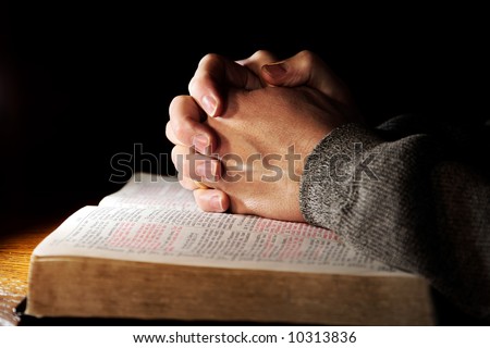 Hands of a man praying in solitude with his Bible (Christian image, shallow focus).